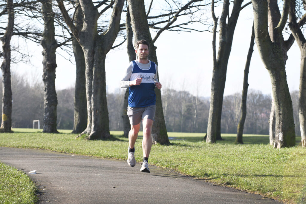 Man wearing Sir Bobby Robson Foundation running vest jogging through a park